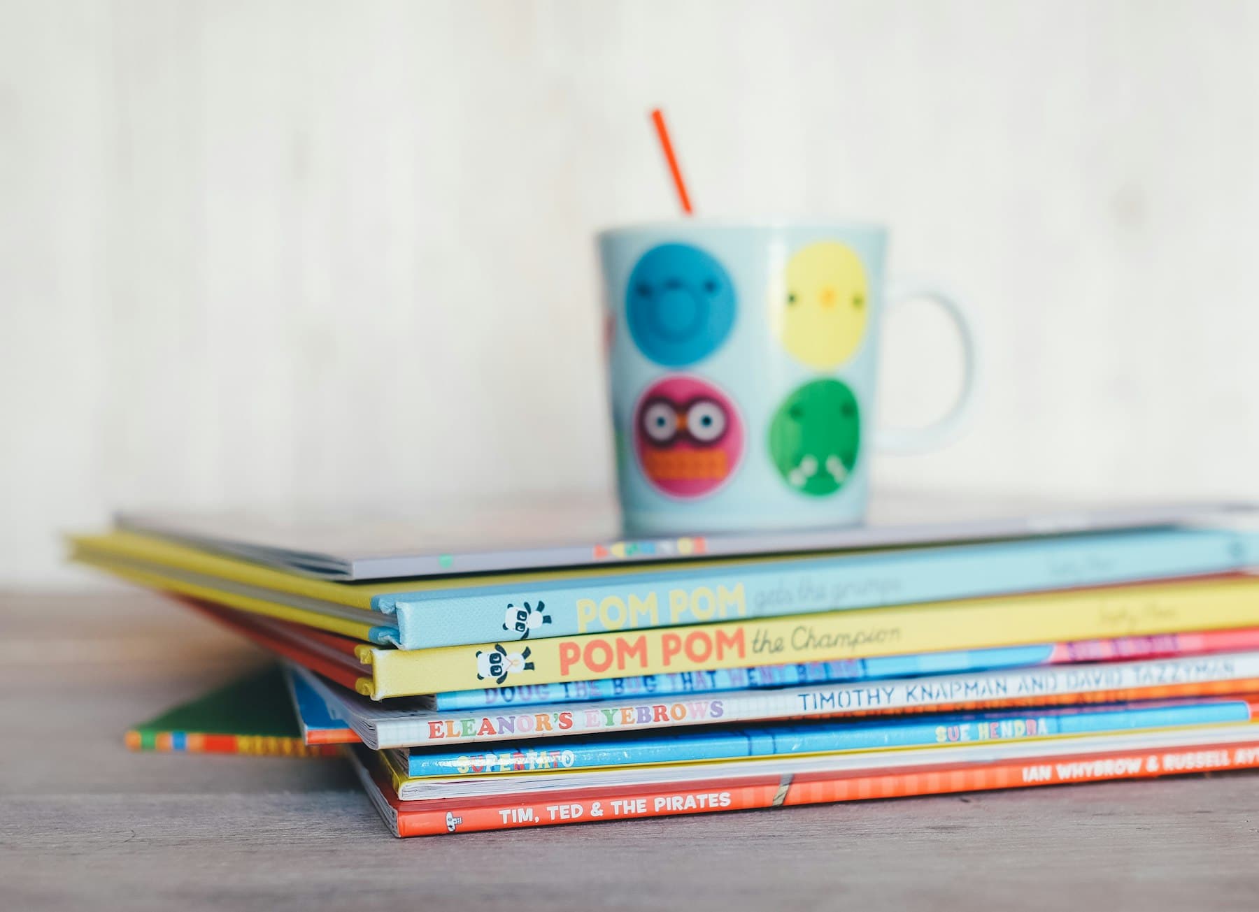 A stack of colourful picture books with a painted mug on top